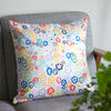 Front view of the daisy cushion cover. With illustrated multi-coloured daisies on a white background. Sitting on a couch. 