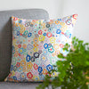 Side view of the daisy cushion cover. With illustrated multi-coloured daisies on a white background. Sitting on a couch. 