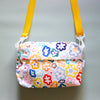 Front view of the Daisy everyday bag. With alternate orange strap. Multicoloured daisy illustrations on a white background. 