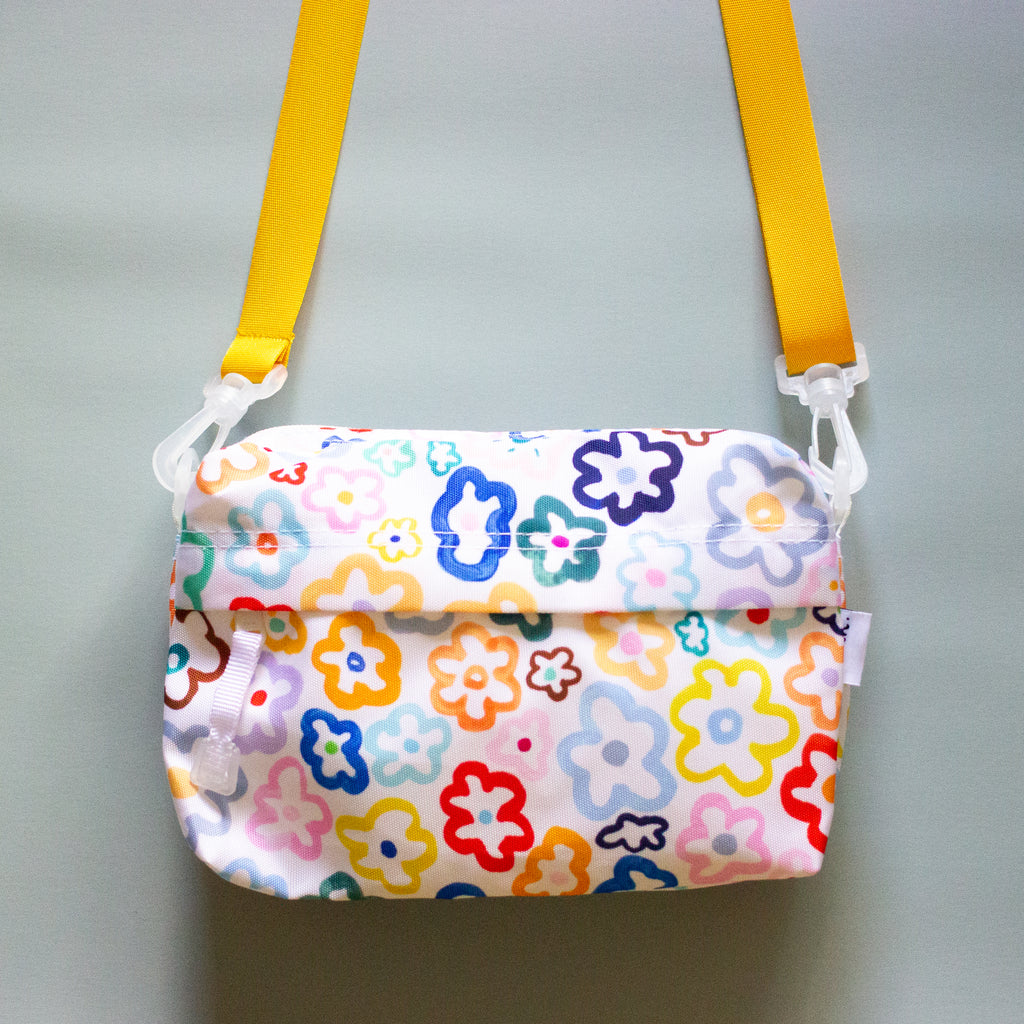 Front view of the Daisy everyday bag. With alternate orange strap. Multicoloured daisy illustrations on a white background. 
