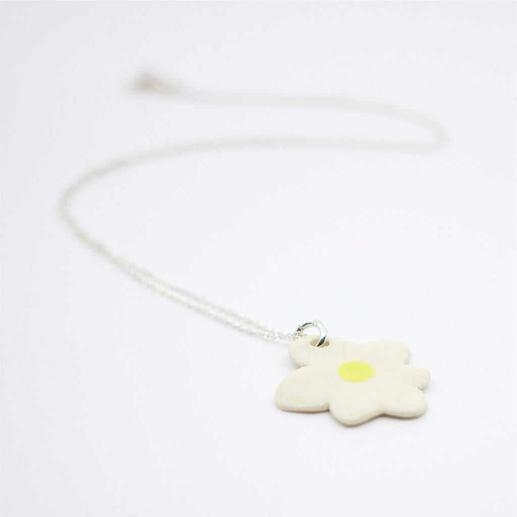 Closeup view of a Sterling silver necklace featuring a large, hand-painted ceramic daisy-shaped pendant with black detailing on a white background.