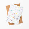 A Back view of the Day Pop greeting card with recycled paper envelope in background. Multicoloured polkadots on a white grid background. 