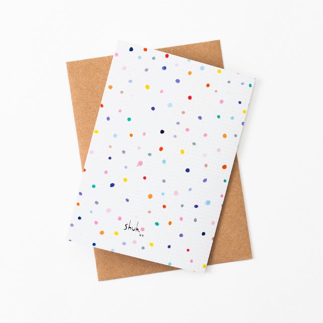 A Back view of the Day Pop greeting card with recycled paper envelope in background. Multicoloured polkadots on a white grid background. 
