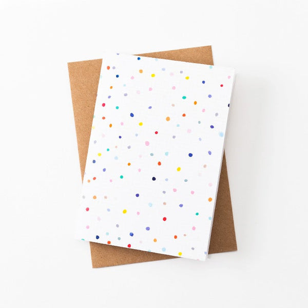 A front view of the Day Pop greeting card with recycled paper envelope in background. Multicoloured polkadots on a white grid background. 