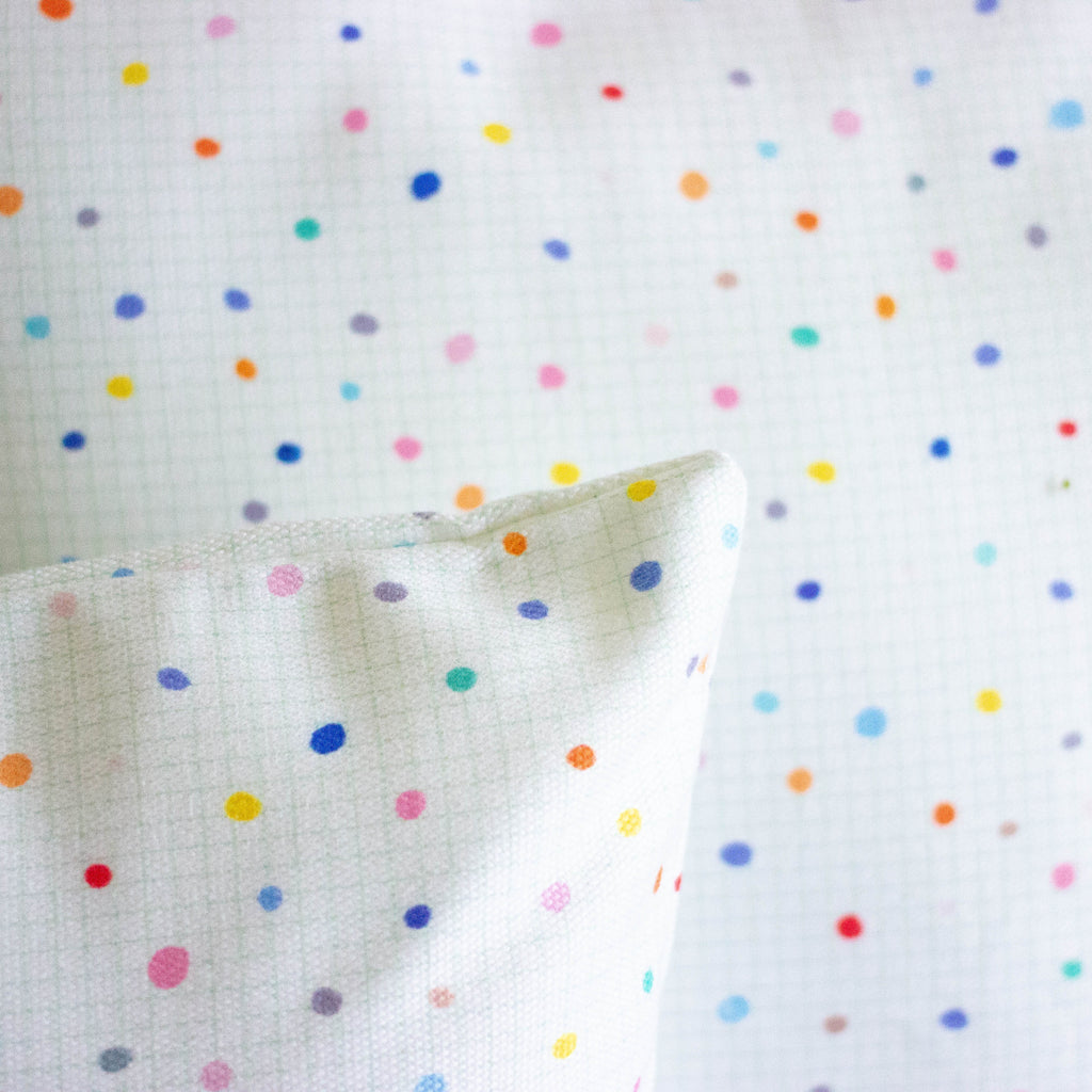 A corner detail view of the day pop cushions. Print is multicoloured polka dots on a light grid background. 
