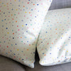A side view of the day pop cushions. Two cushions on a couch. Print is multicoloured polka dots on a light grid background. 
