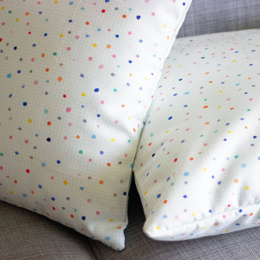 A side view of the day pop cushions. Two cushions on a couch. Print is multicoloured polka dots on a light grid background. 