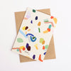 Back view of the enough card, with recycled paper envelope. Print features colourful patches and splotches. 