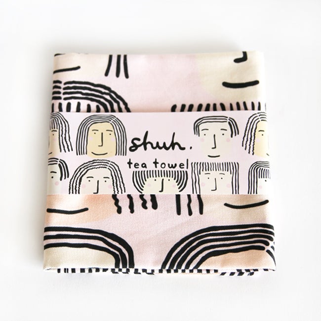 Fab faces tea towel. Different diverse faces, with different features, on a pink background. With the packaging. 