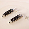 Flat view of a Pair of handmade ceramic earrings shaped like fish with a black check pattern and tiny white faces, finished with silver stud backings. Designed by shuh.
