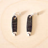 Pair of handmade ceramic earrings shaped like fish with a black check pattern and tiny white faces, finished with silver stud backings. Designed by shuh.