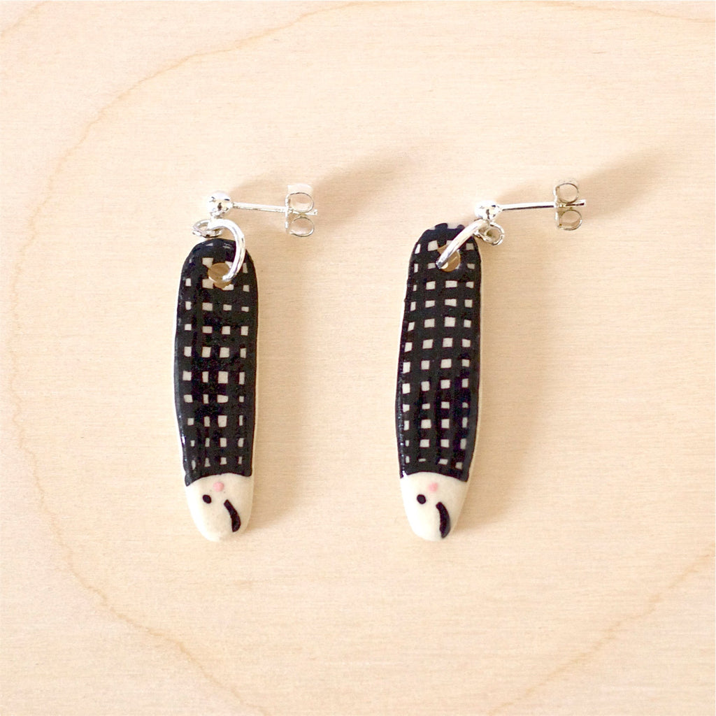 Pair of handmade ceramic earrings shaped like fish with a black check pattern and tiny white faces, finished with silver stud backings. Designed by shuh.