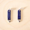 Pair of handmade ceramic earrings shaped like fish with a navy blue check pattern and small face details, finished with silver stud posts. Designed by shuh.