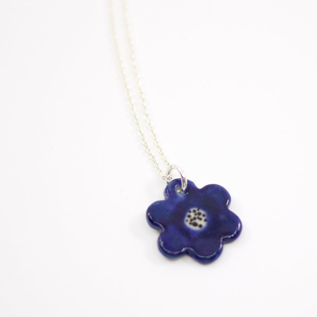 Closeup view of the Sterling silver necklace with a hand-painted ceramic blue flower-shaped pendant, featuring black line detail, displayed on a white background.