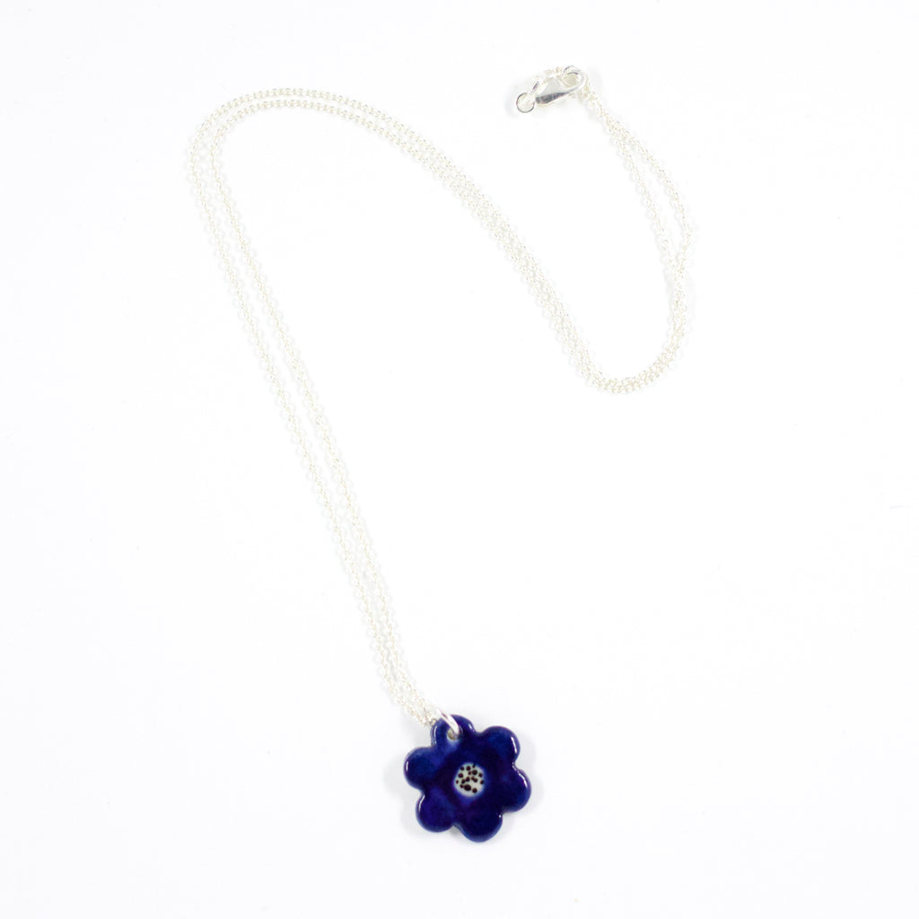 Sterling silver necklace with a hand-painted ceramic blue flower-shaped pendant, featuring black line detail, displayed on a white background.
