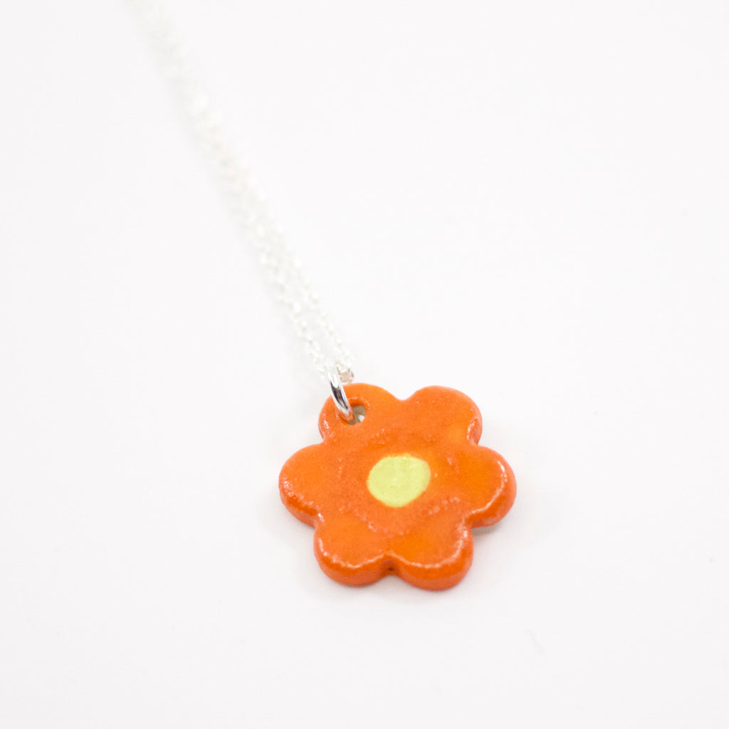 Sterling silver necklace with a glossy orange ceramic flower-shaped pendant featuring a yellow dotted centre, displayed on a white background.