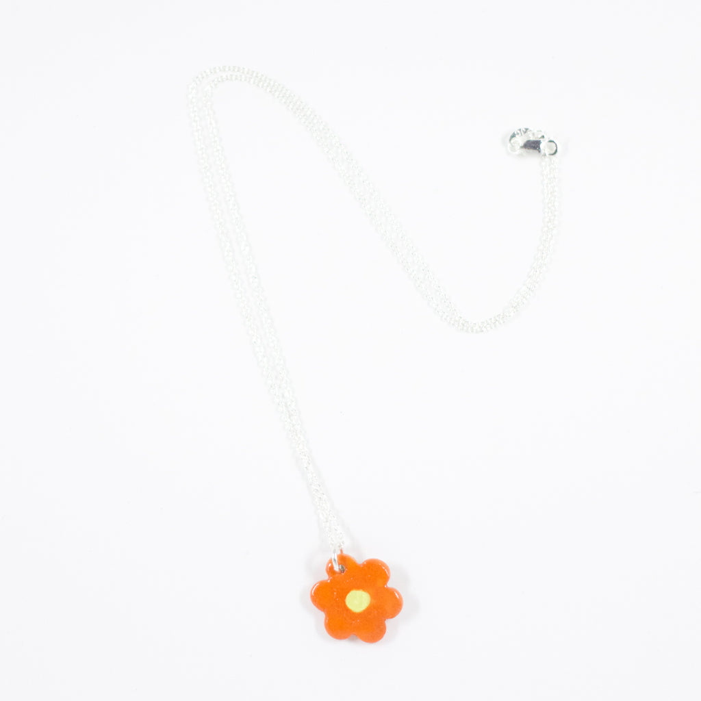 Sterling silver necklace with a glossy orange ceramic flower-shaped pendant featuring a yellow dotted centre, displayed on a white background.