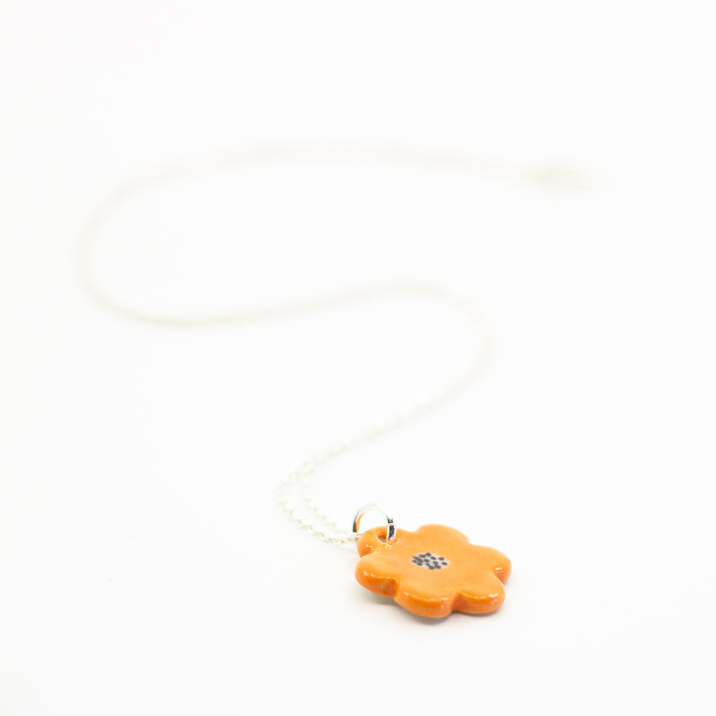 Sterling silver necklace featuring a bright orange ceramic flower-shaped pendant with a black dotted centre, displayed on a white background.
