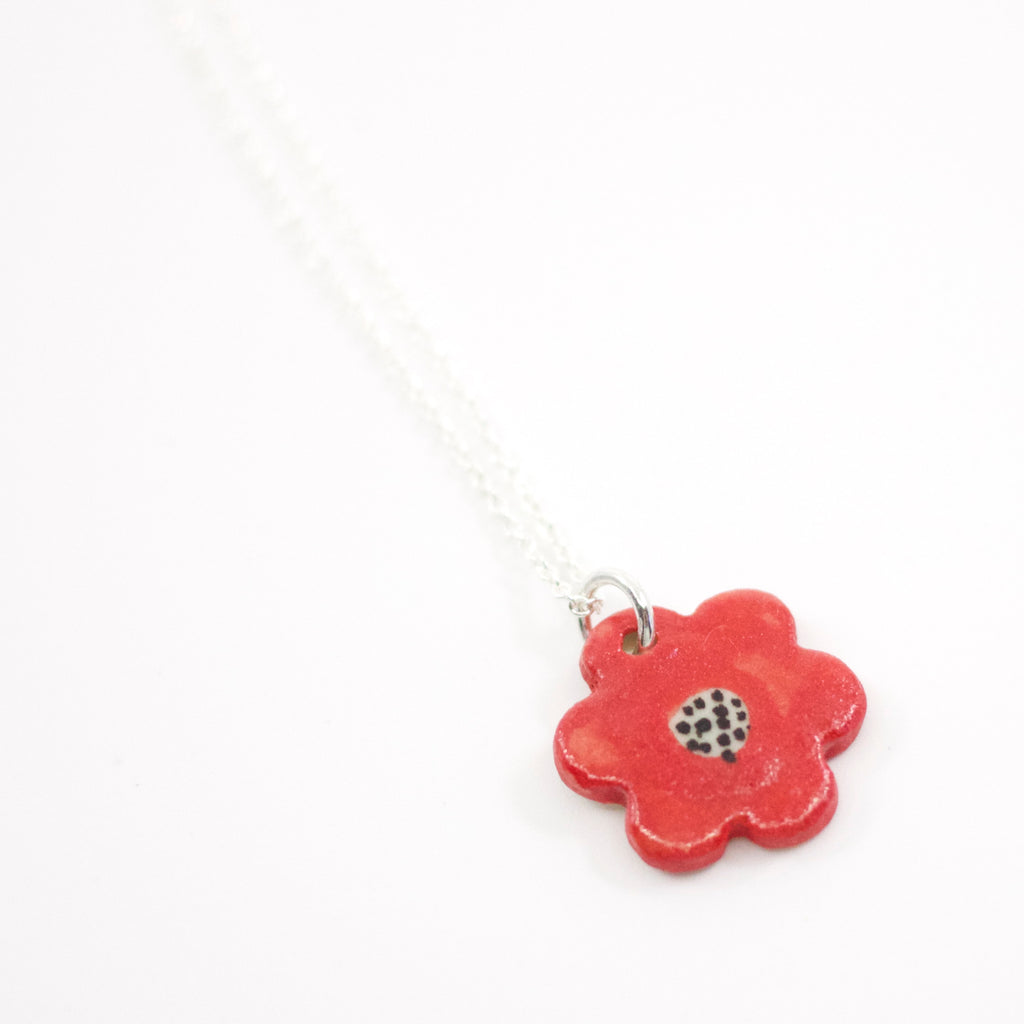 Closeup of the Sterling silver necklace featuring a red hand-painted ceramic flower pendant with black line detailing, displayed on a white background.