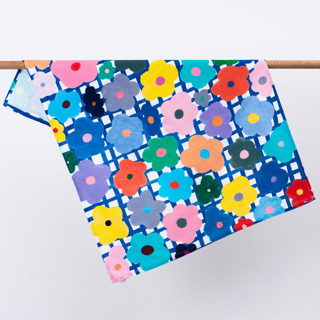 The flower tea towel, hanging from a rack. Bright multicoloured flowers on a blue and white chequered background. 