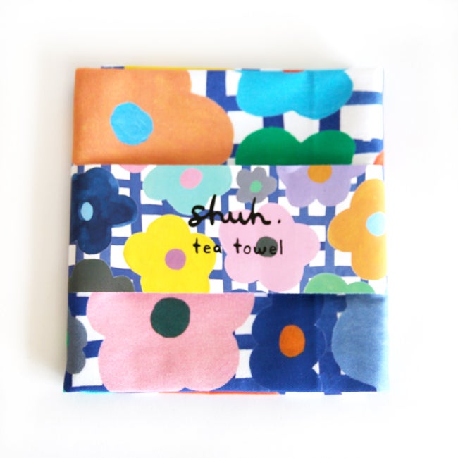 The flower tea towel, in packaging. Bright multicoloured flowers on a blue and white chequered background. 