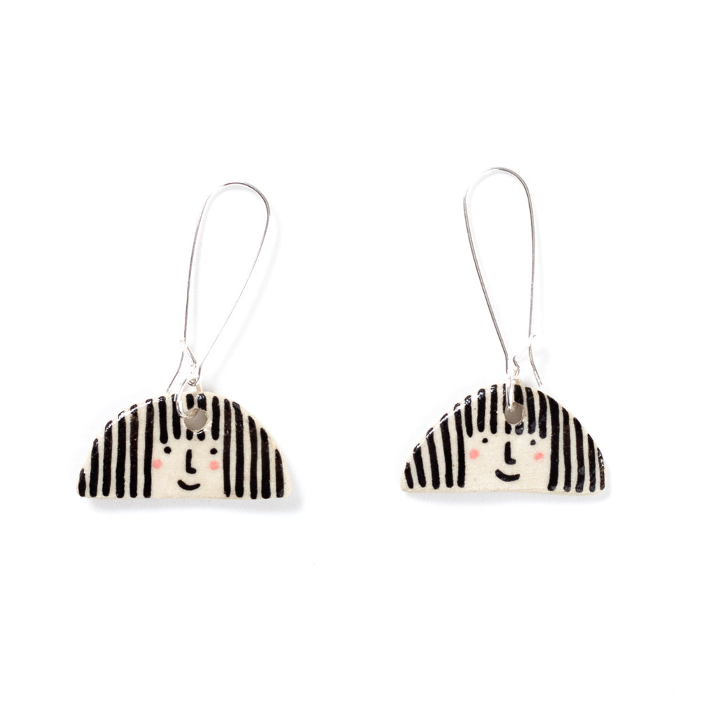 Two ceramic drop earrings with sterling silver long hook. Ceramic pendant has a girl face with pink cheeks, stripey hair and smile. 