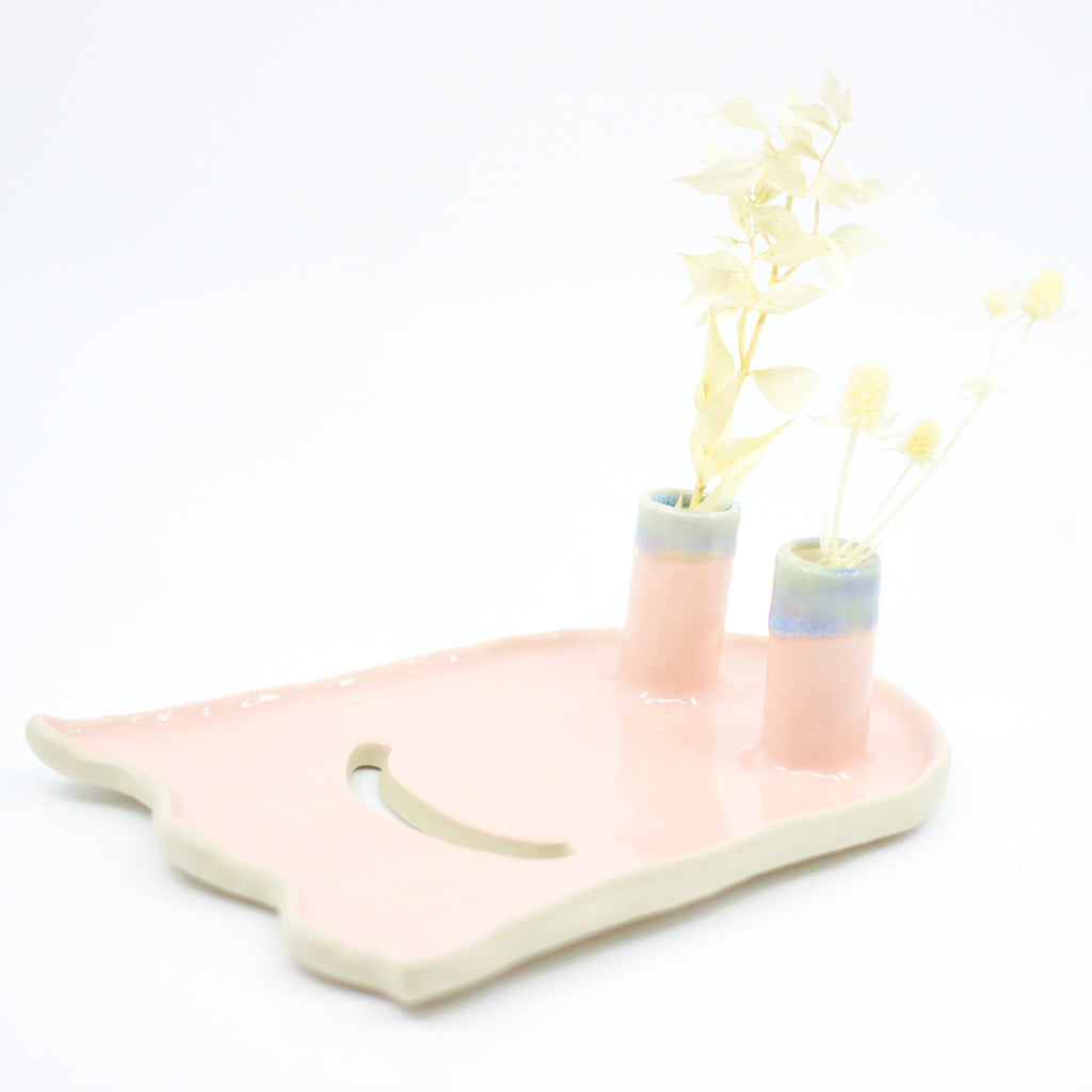 Side view of the ghost trinket dish. Two spouts hold flowers. Dish is ghost shaped. Pink colour, and a cutout smile. 