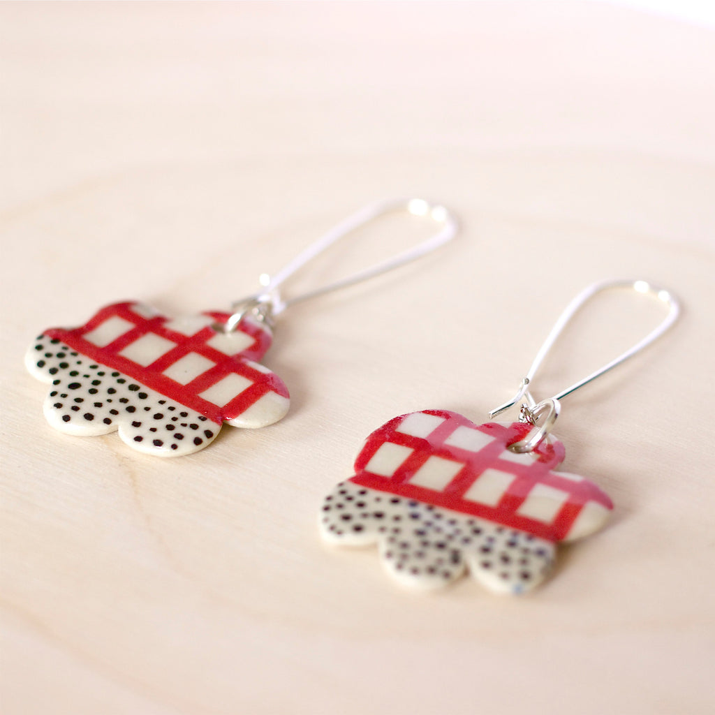 Cloud shaped ceramic bead earrings with rope attachment stitched with yellow fabric binding. Ceramic bead has red lines and black spots patterns on it. 