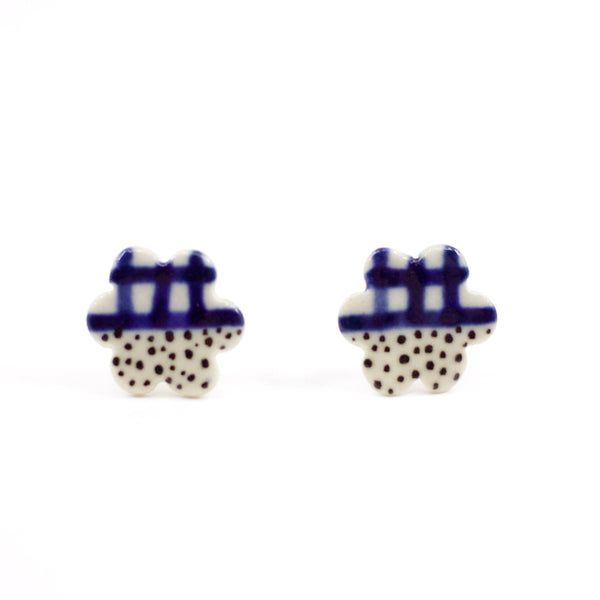 Pair of handmade ceramic stud earrings in a flower-like shape with indigo check pattern on top and black speckles on the bottom. Designed by shuh.