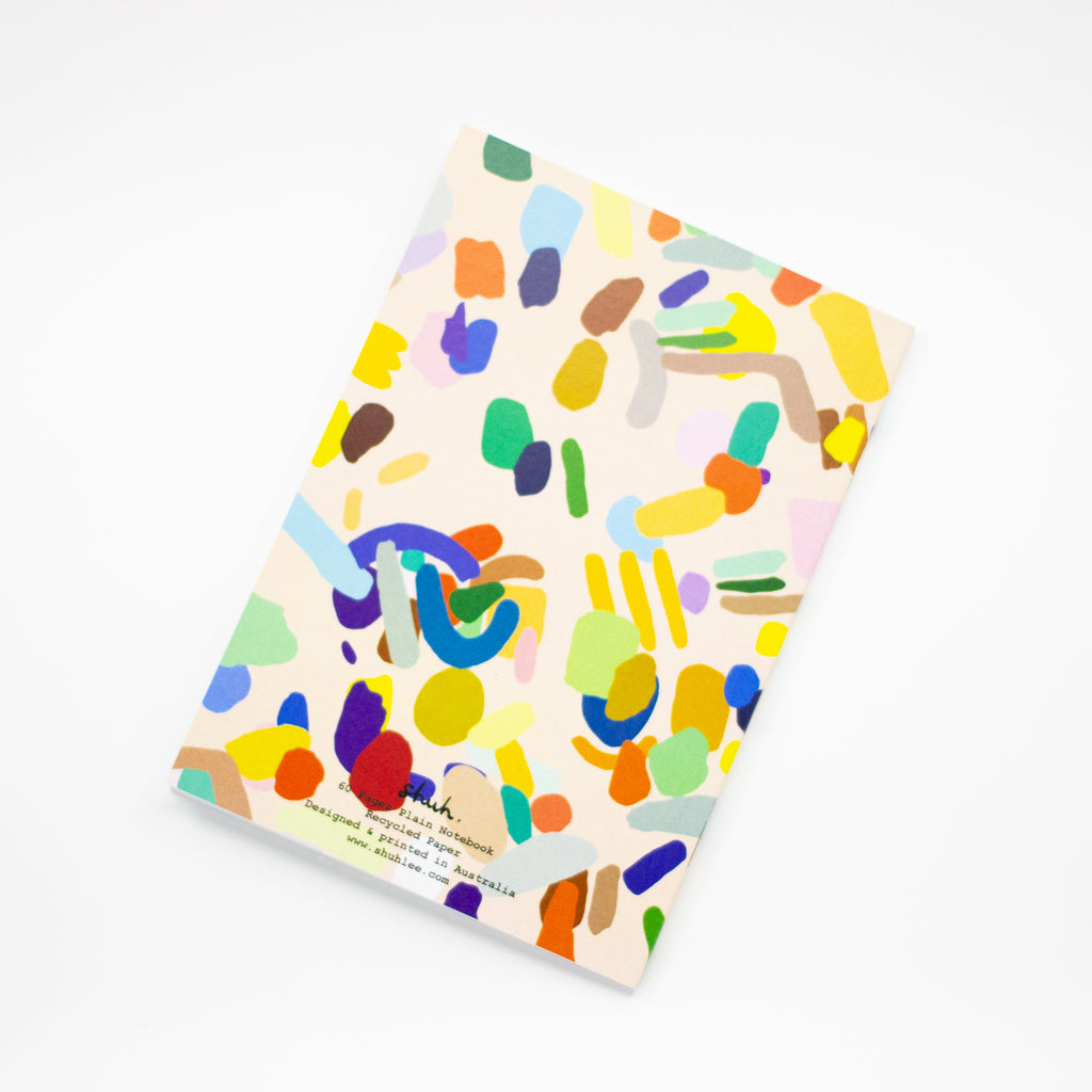 Back view of the Hanging Out notebook. Cover features multicoloured shapes on a light background. Open to show blank pages inside. 