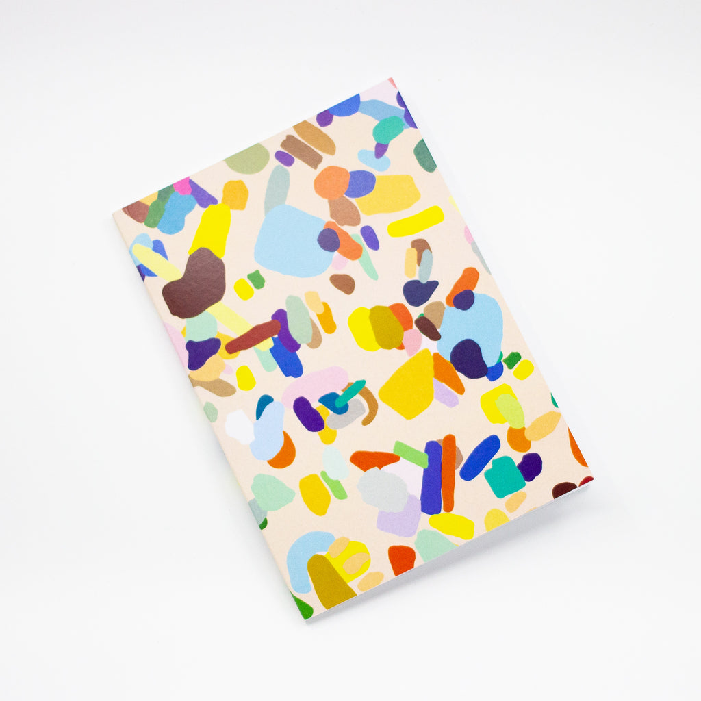 Front view of the Hanging Out notebook. Cover features multicoloured shapes on a light background. 