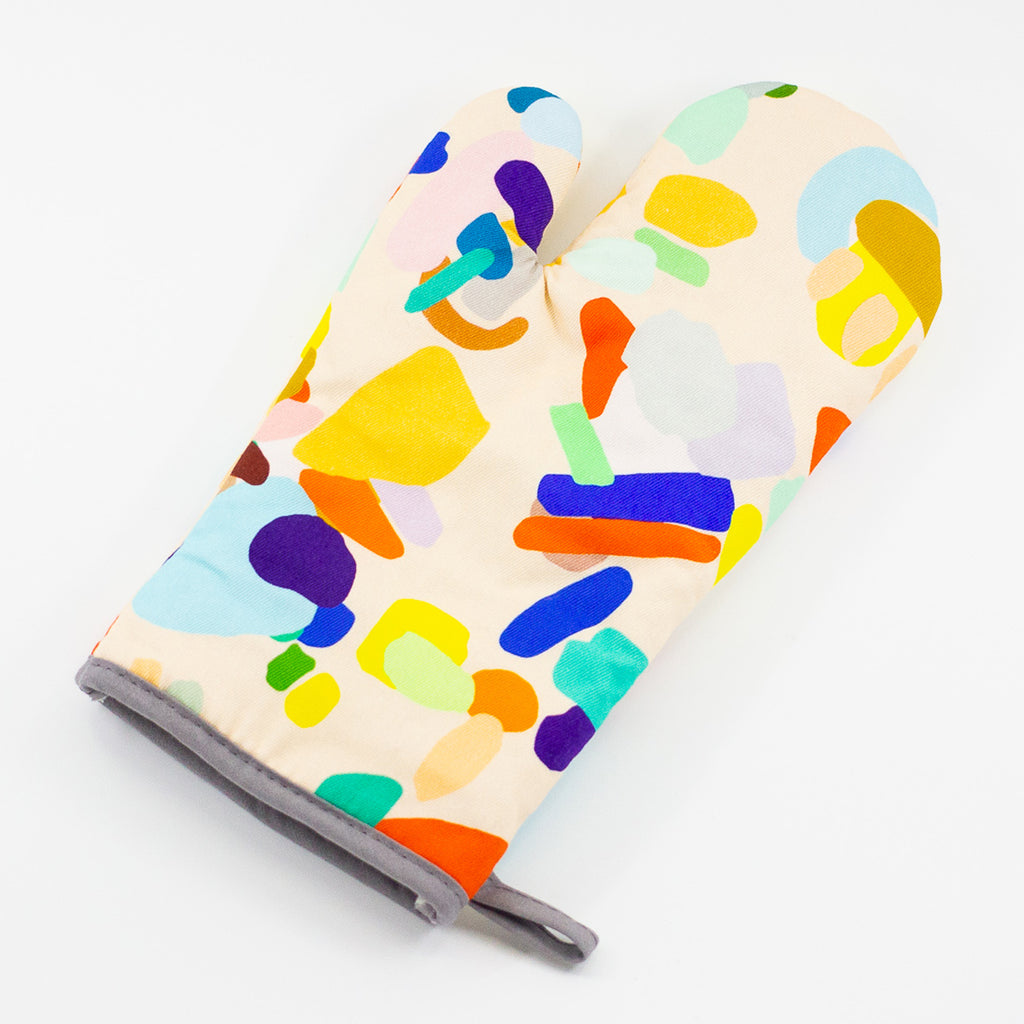 A top view of the Hanging Out oven mitt. Abstract shapes with multi coloured designs on a light background. 
