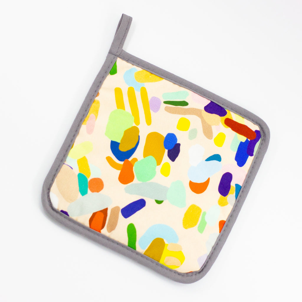The Hanging Out pot holder front view. Multicoloured abstract design on a peach background. 