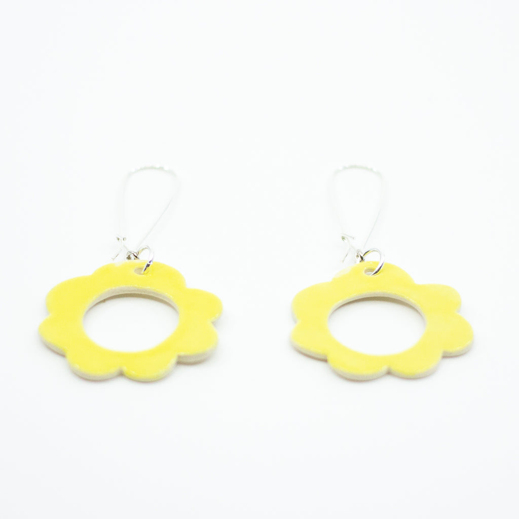 Flat view of two ceramic drop earrings, with sterling silver hooks. Ceramic pendants are circular flower shaped with a hollow centre. Hand painted yellow. 