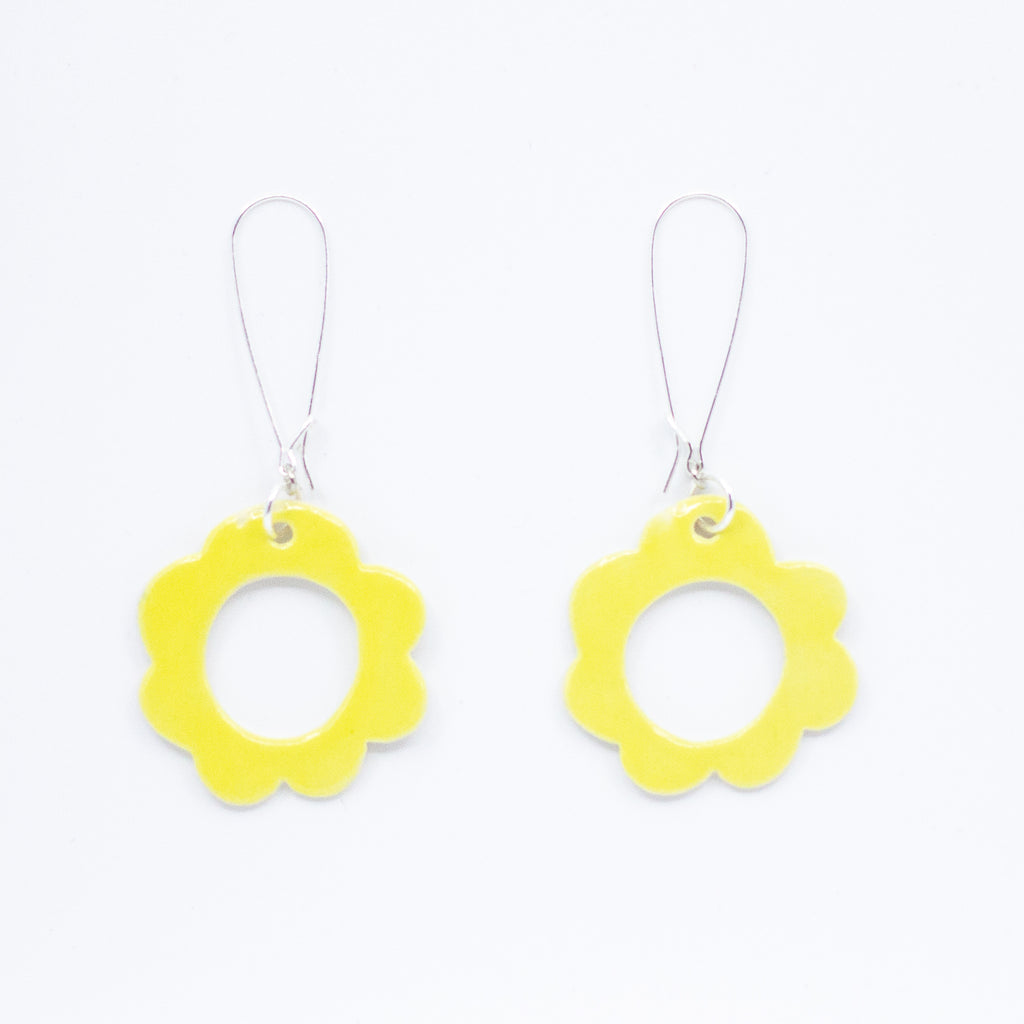 Two ceramic drop earrings, with sterling silver hooks. Ceramic pendants are circular flower shaped with a hollow centre. Hand painted yellow. 