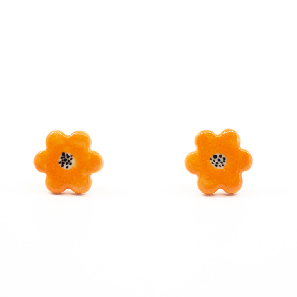 A pair of handmade ceramic stud earrings shaped like orange flowers, each with a speckled black centre. Finished with Sterling Silver posts.