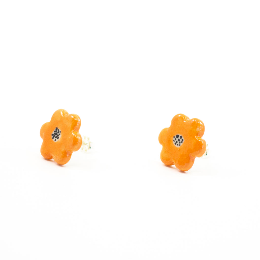 Side view of a pair of handmade ceramic stud earrings shaped like orange flowers, each with a speckled black centre. Finished with Sterling Silver posts.