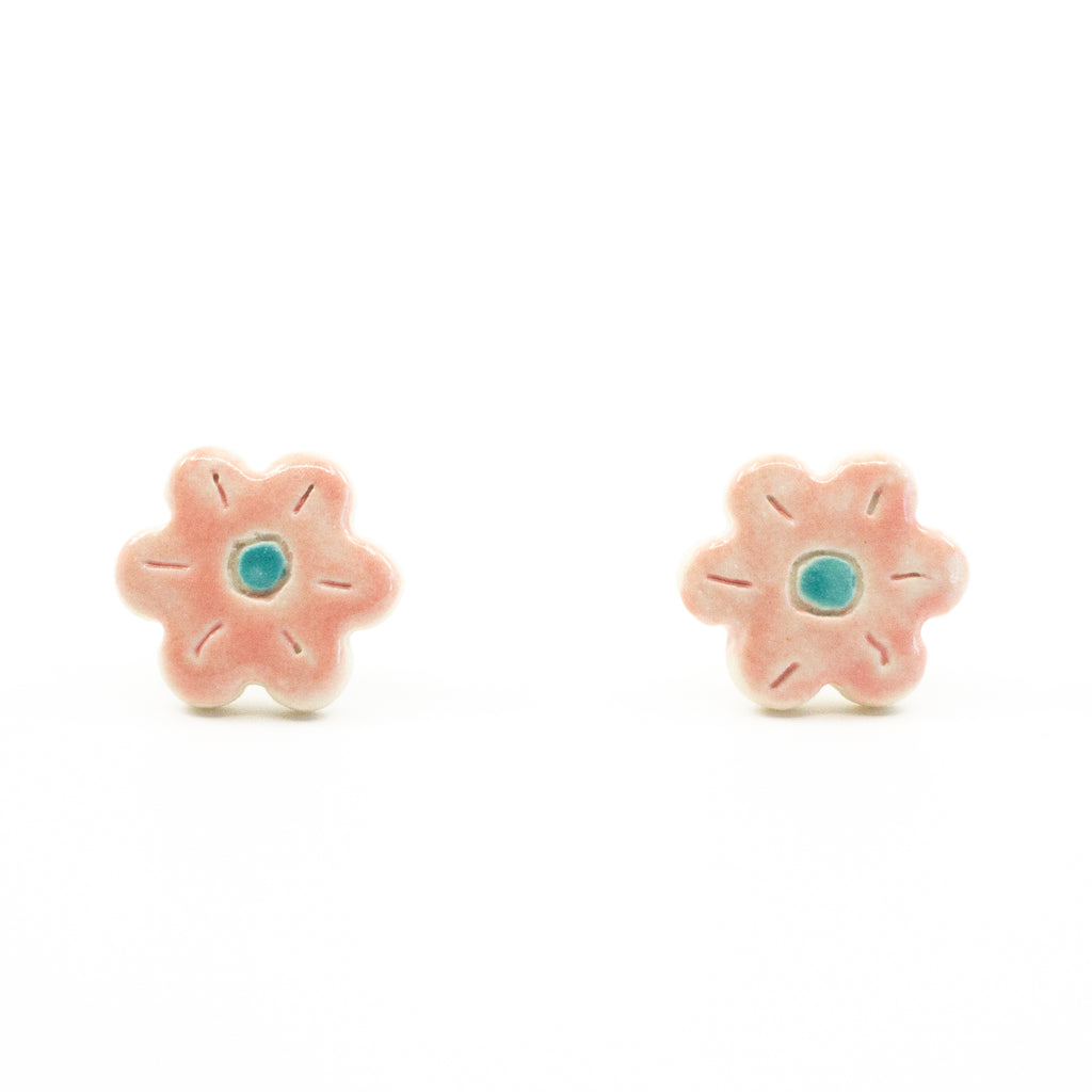 A pair of handmade ceramic stud earrings shaped like pink flowers, featuring carved petal details and a teal blue centre. Finished with Sterling Silver posts.