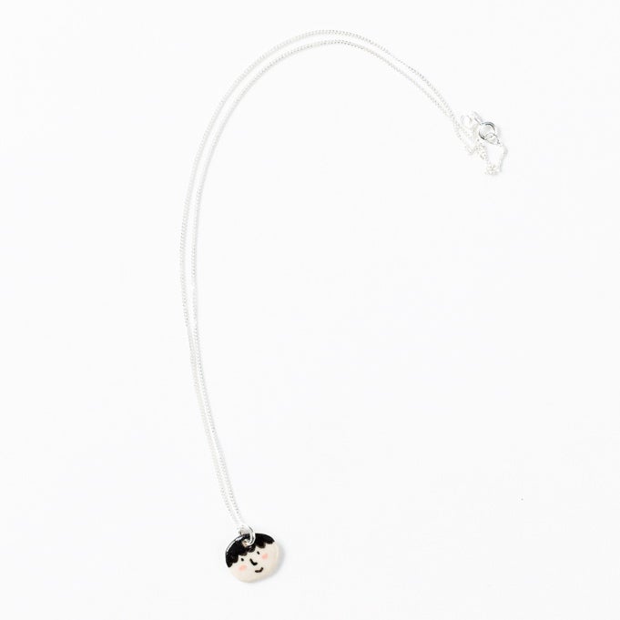 Sterling silver necklace featuring a small, hand-painted ceramic pendant with a playful face design, displayed on a white background.