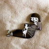 Closeup details of an Enamel pin featuring a hand-drawn girl character playing with a puppy dog, 