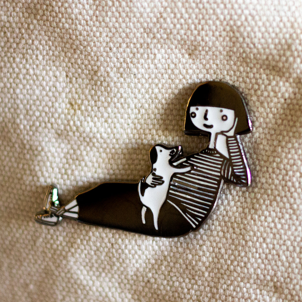 Closeup details of an Enamel pin featuring a hand-drawn girl character playing with a puppy dog, 
