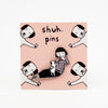 Enamel pin featuring a hand-drawn girl character playing with a puppy dog, displayed on pink card with dog illustrations and “shuh. pins” branding.