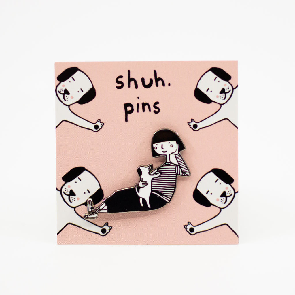 Enamel pin featuring a hand-drawn girl character playing with a puppy dog, displayed on pink card with dog illustrations and “shuh. pins” branding.
