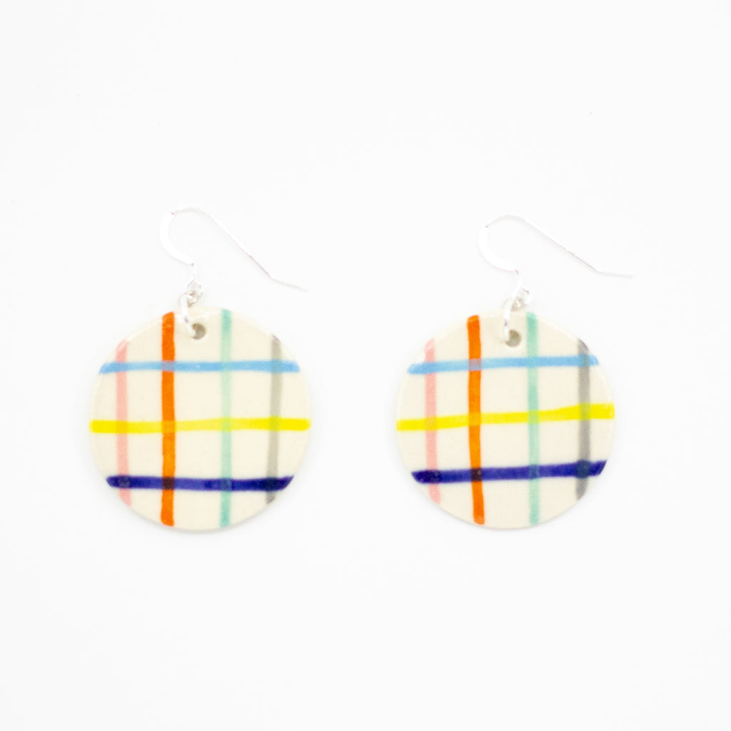 A pair of handmade ceramic earrings with round drops, painted in a rainbow grid pattern of colourful vertical and horizontal stripes. Finished with silver hooks for pierced ears.