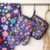 Salad tea towel, oven mitt, and pot holder.  front view. Flowers and polkadots, all multicoloured, on a navy background. 
