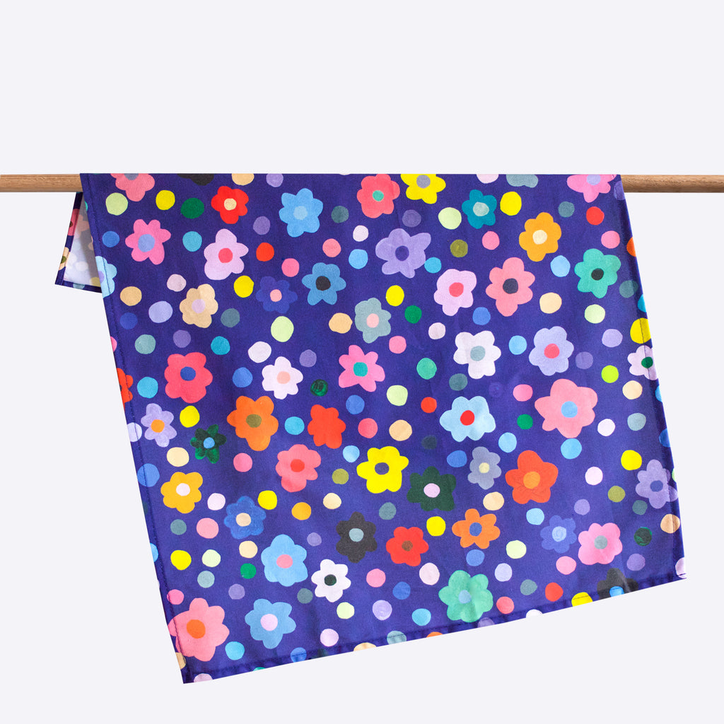 Salad tea towel, front view. Flowers and polkadots, all multicoloured, on a navy background. 