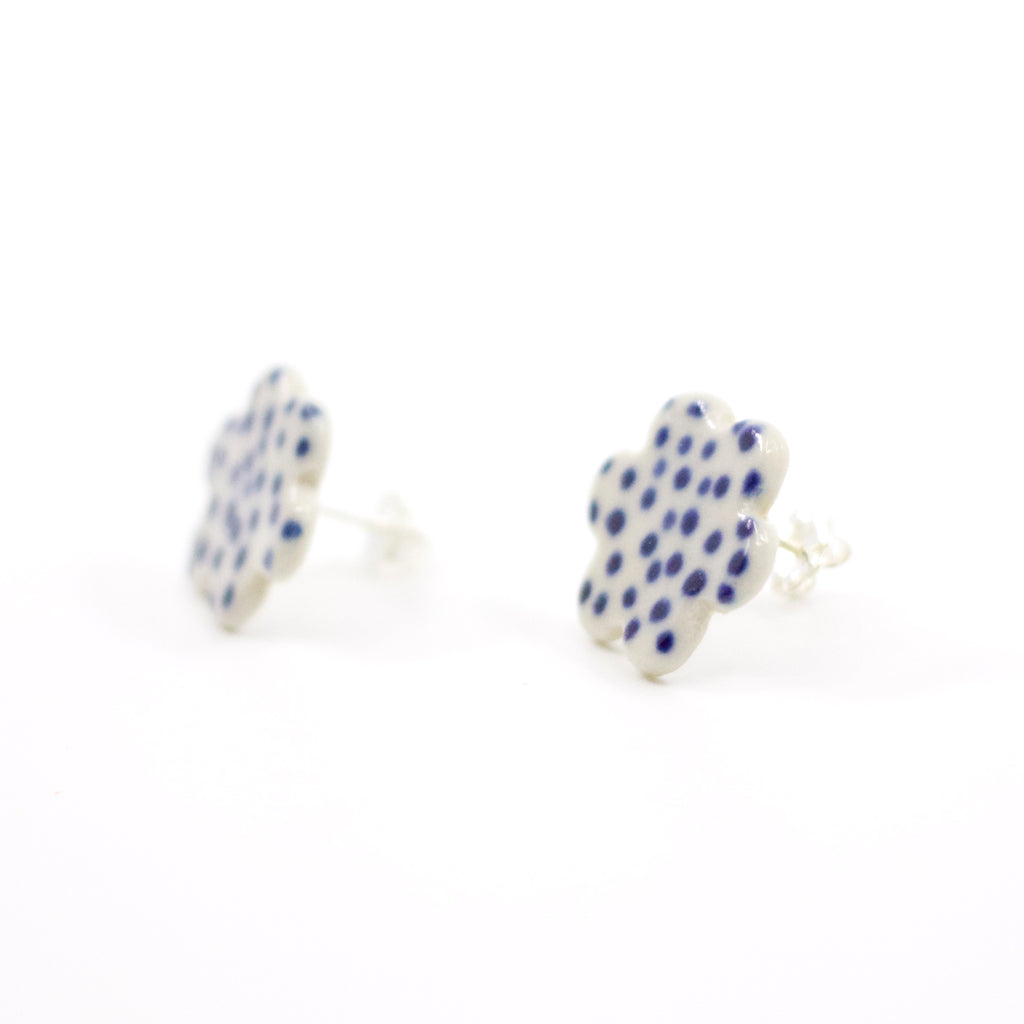 Side view of a pair of handmade ceramic stud earrings shaped like small clouds with an indigo blue dotted pattern on white. Sterling silver studs.  Designed by shuh.