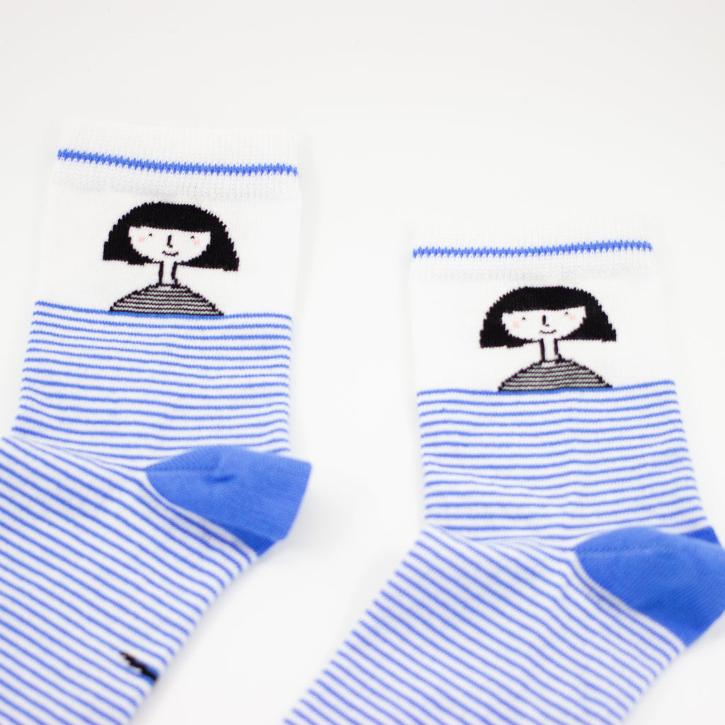 A closeup cuff view of the shuh. girl socks. Featuring the iconic shuh. girl and a blue and white striped pattern, these socks are designed to bring fun and imagination to your feet