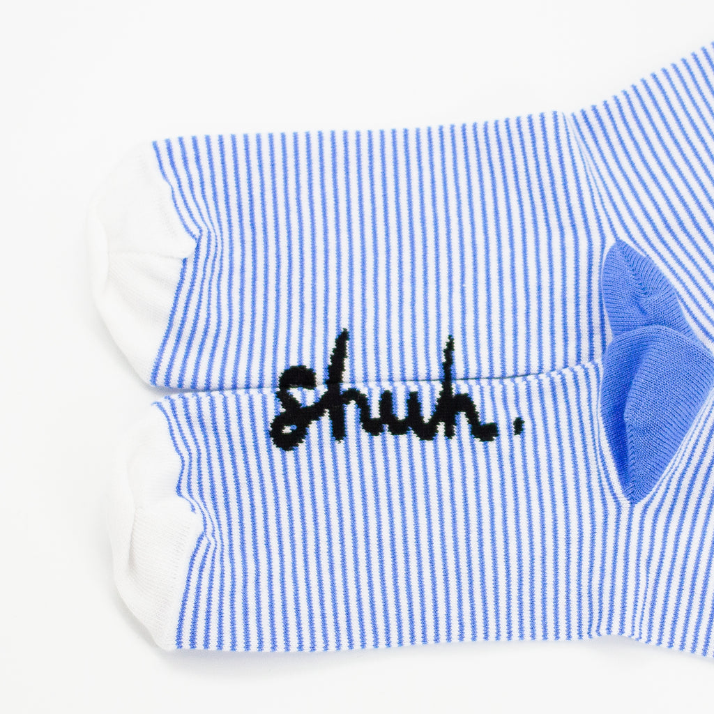 View of the sole of the shuh. girl socks. Featuring the iconic shuh. girl and a blue and white striped pattern, these socks are designed to bring fun and imagination to your feet