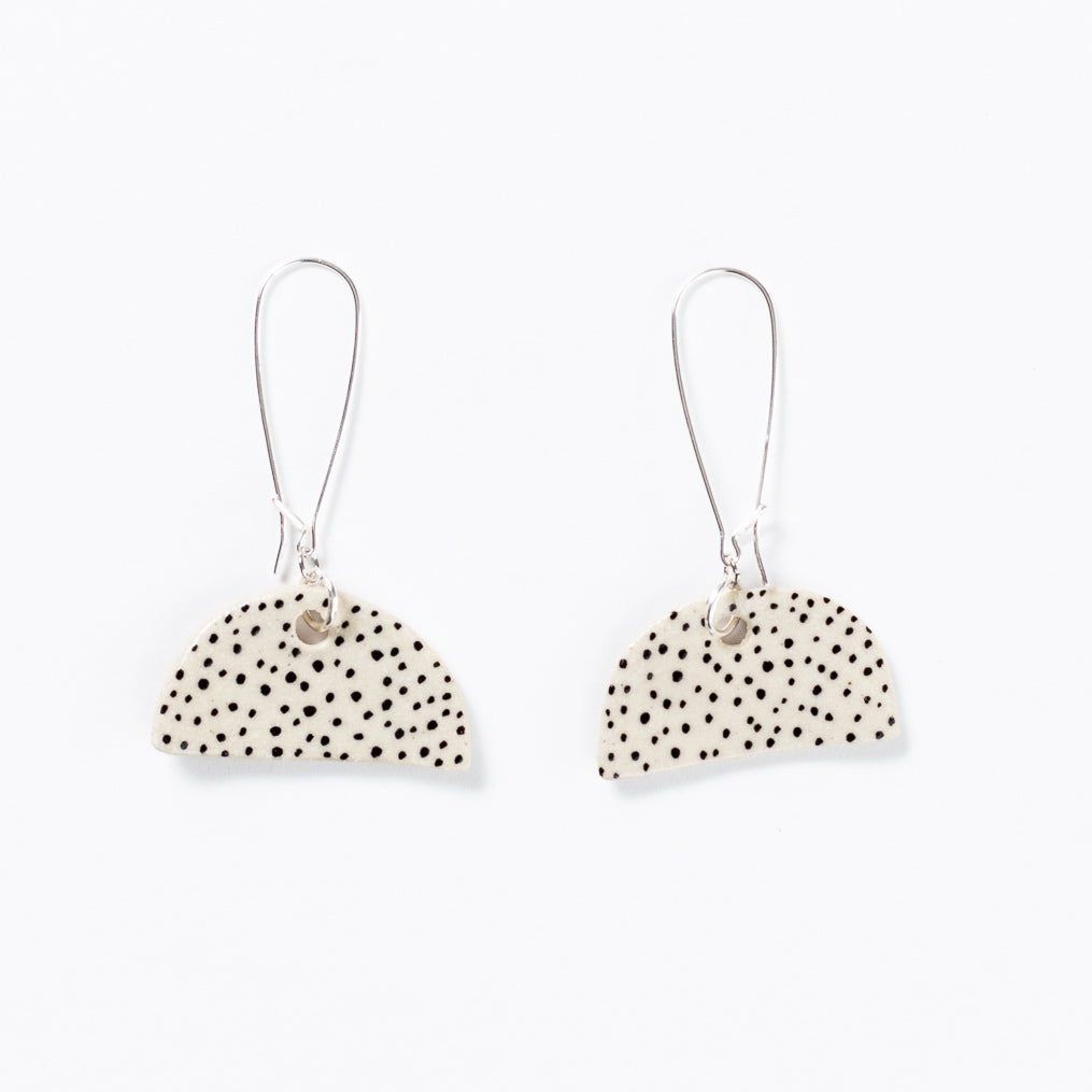 Two ceramic drop earrings with long sterling silver hooks. Ceramic pendant is half moon shaped with hand drawn polka dots. 